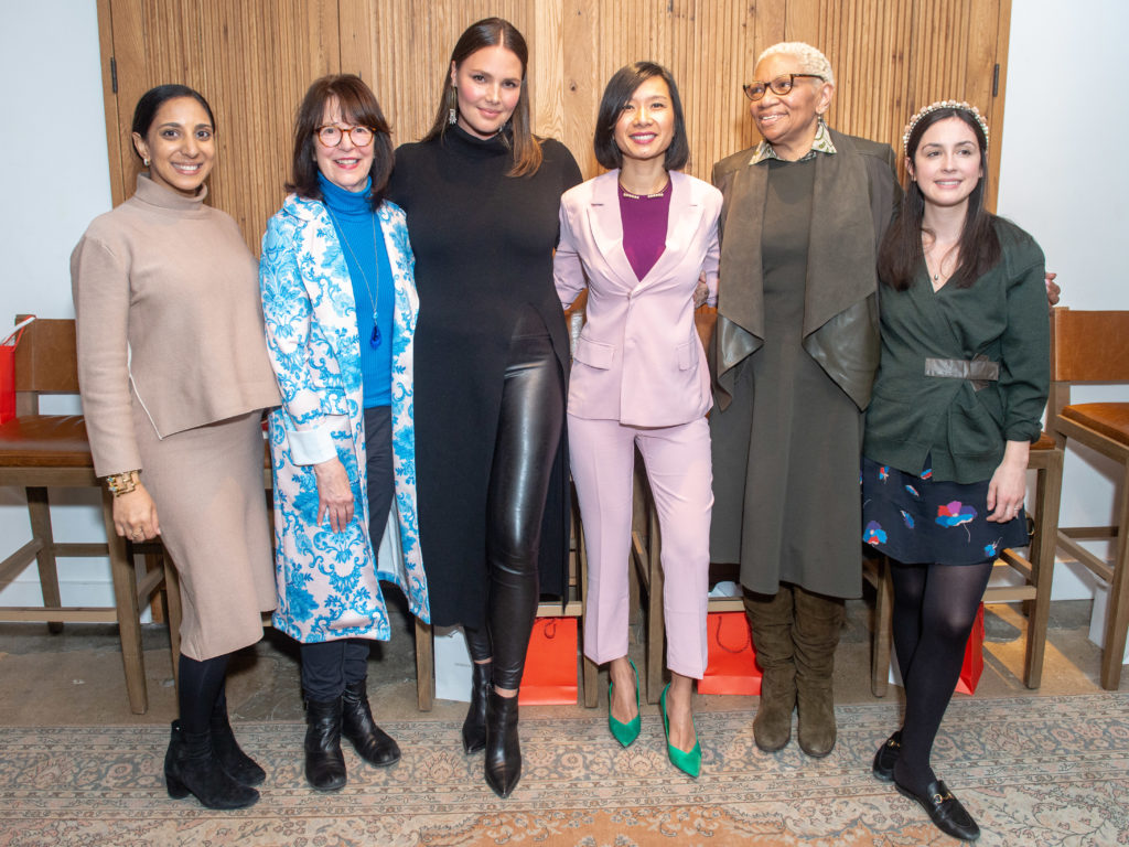Six women standing in a row at an event.